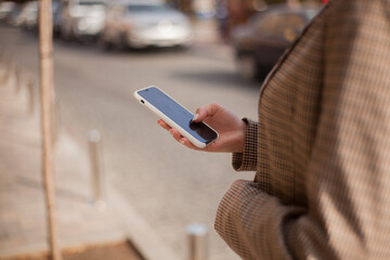 close-up of a girl's hand in a suit prints a business message on her smartphone against the background of the city