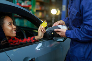 Female customer made a payment on the car by giving a credit card to the male mechanic in the garage.