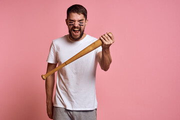 Emotional man with a baseball bat in his hand on a pink background and black lines on the face of the model grimace