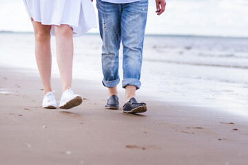 male and female legs in sports shoes walk along the beach against the background of the sea.