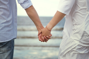 man and woman are holding hands, walking against the background of the sea.