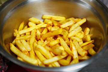 Fried French fries in metal bowl.Unhealthy junk food prepared in deep fryer oven for dinner in American restaurant.Traditional potato chips cooked in hot oil.Golden potatoes prepared with deep-frying