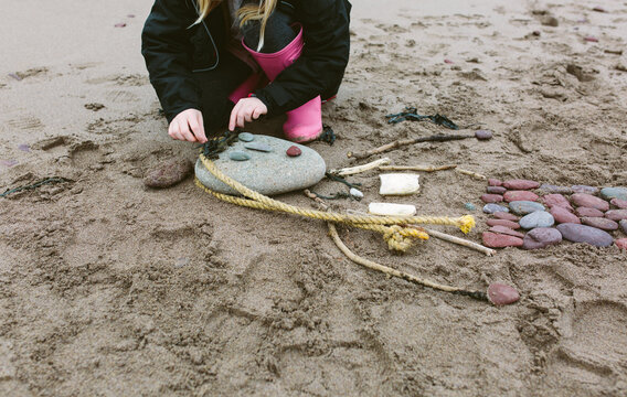A little girl making a mermaid from pebbles and other beach finds on a beach in winter