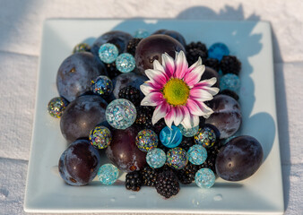 Composition of pink daisy on a plate with blue spherical objects