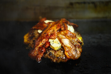 Minced beef patty with blue gorgonzola cheese & bacon strips frying on hot pan in American fast food restaurant for dinner