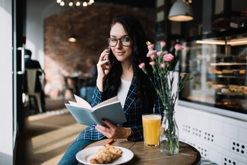 Female student with book talking on cellphone in cafe