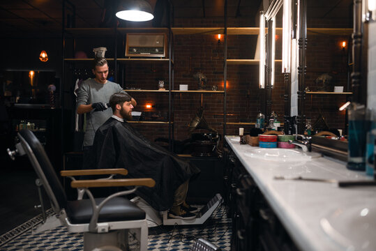 Caucasian male hairdresser trimming client's hair at barbershop