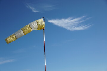 Yellow-white wind sock on the blue sky background.