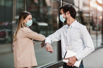 Business man and woman with safety masks greeting with elbow bump in front of office building.
