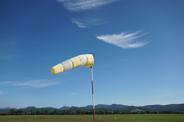 Yellow-white wind sock on the blue sky background.