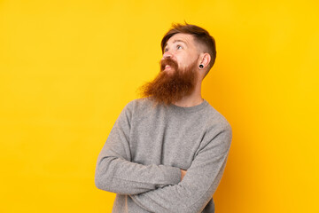Redhead man with long beard over isolated yellow background looking up while smiling