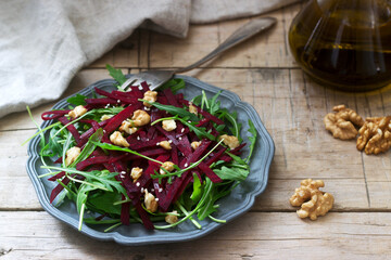 Vitamin salad of raw beets, arugula, walnuts and olive oil on a wooden table. Rustic style.