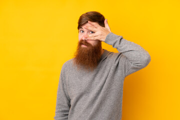 Redhead man with long beard over isolated yellow background covering eyes by hands and smiling