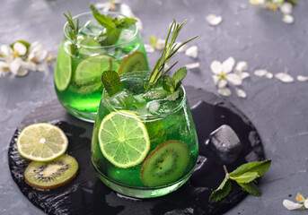 Non-alcoholic Mojito cocktail in a glass with syrup, fresh mint, lime and kiwi slices, sparkling water with ice. It has a citrus aroma and pleasant taste.