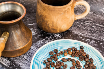 Clay cup with cezve and coffee beans on a blue saucer. Coffee concept