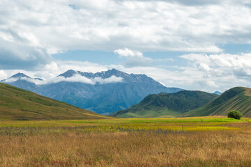 View to Tien Shan mountains from summer valley. Summer day, blue sky, white clouds