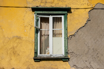 Vintage green wooden window on the facade of an yellow old house. The plaster on the wall is partially damaged