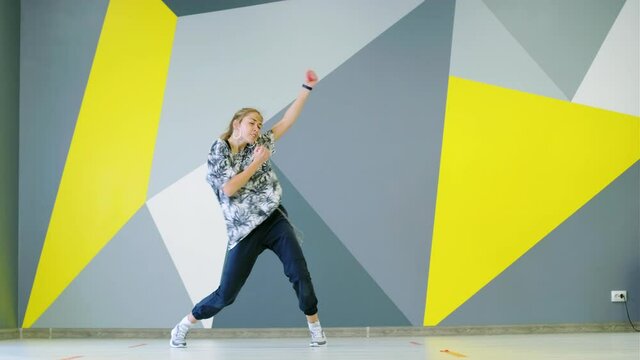 Cheerful young girl dancing hip hop in the studio in front of the wall with bright geometric pattern.