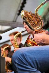 Detailansicht der Ventile und Windungen eines Baritonsaxofons während eines Big Band Konzertes. Unscharfe Musiker im Hintergrund. Sax Section of Bigband in concert. Stage view with musicers.