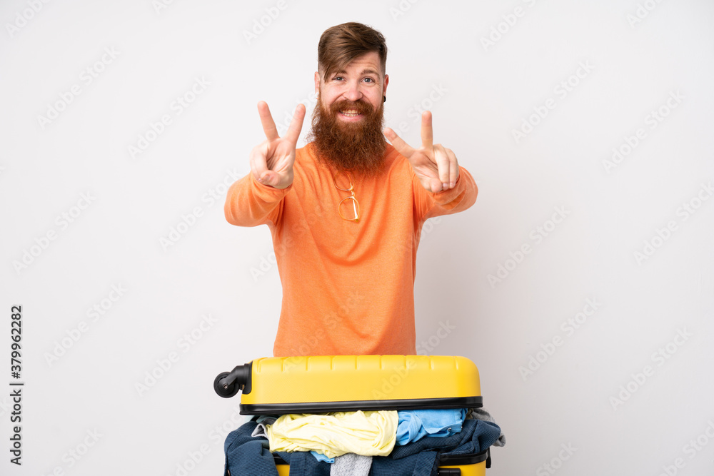 Wall mural traveler man with a suitcase full of clothes over isolated white background smiling and showing vict