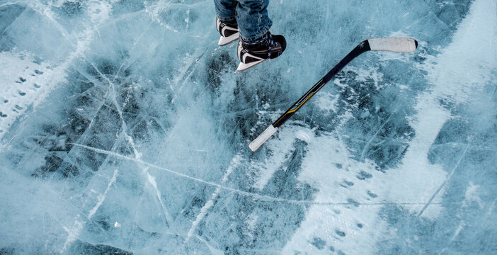 A child stands next to a hockey stick on a frozen pond.