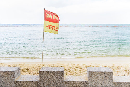 Waving flag with text swim here on beach