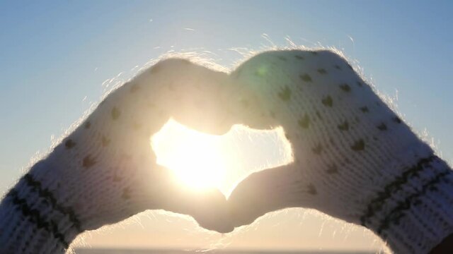 The girl made a love heart from hands in mittens. Lady making a heart shape with her hands. Shining summer sun on your hands. Sunbeams on the morning weekend. Winter time.
