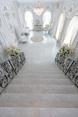 luxury royal posh interior in baroque style. very bright, light and white hall with expensive oldstyle furniture. chic wide marble staircase leading to the second floor