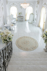 luxury royal posh interior in baroque style. very bright, light and white hall with expensive oldstyle furniture. chic wide marble staircase leading to the second floor
