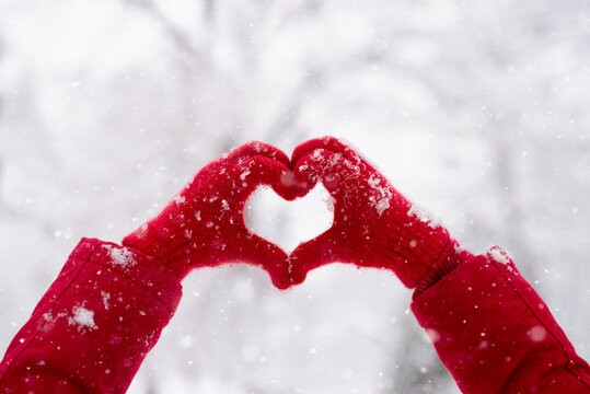 Woman making heart symbol with snowy gloves