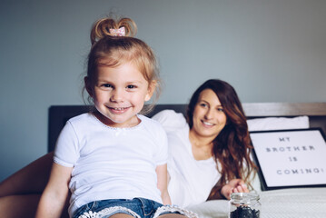 Happy daughter playing with her pregnant mother, on background a letter board written My Brother is Coming