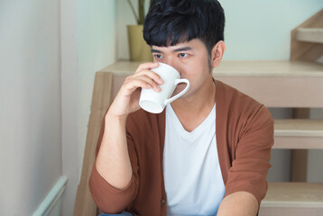 A handsome man wearing knitted coat drinks coffee and looks out the window. Enjoy working day field...