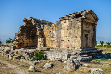 Fototapeta premium Antique crypt in necropolis of antique city Hierapolis, Pamukkale, Turkey. It was belonged to noble family. Entrance decorated with traditional portico, one of walls damaged. Roof overgrown with weeds