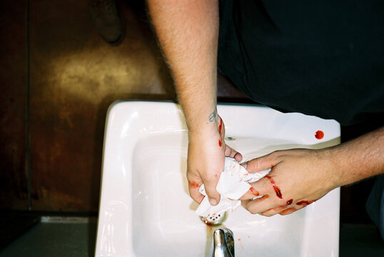 young male washes blood of hands in sink