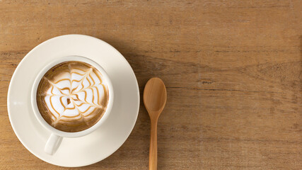hot latte coffee and bubble in white coffee cup and saucer with spoon on wooden background.top view,flat lay,top down.