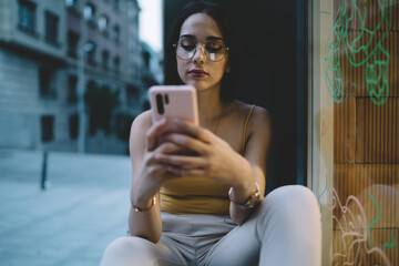 Obraz premium Young woman chatting via smartphone on street windowsill