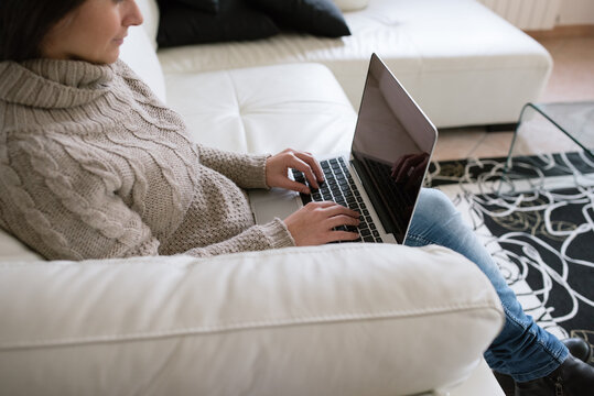 Side view of a woman using a laptop on a sofa