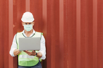 Portrait of logistic engineer man foreman wearing protective mask using laptop checking stock product working at container warehouse construction site. New normal working lifestyle preventing virus