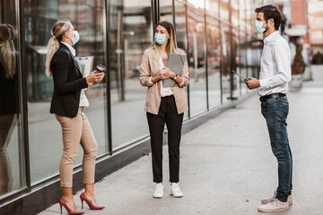 Three employers standing in social distance wearing face mask looking at each other and talking