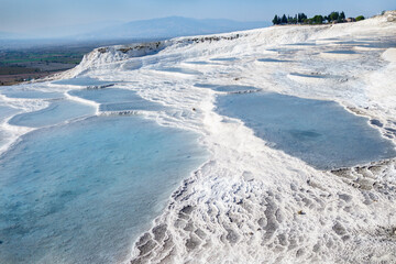Naklejka na ściany i meble Snow white travertine terraces of Pamukkale, Turkey. Pools filled with water from hot spring. Structure created by calcium carbonate mineral. Site is popular among tourists & it's included in UNESCO