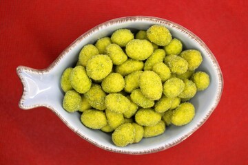 crunchy peanuts coated with wasabi ready for finger food served in a light blue bowl on a red background
