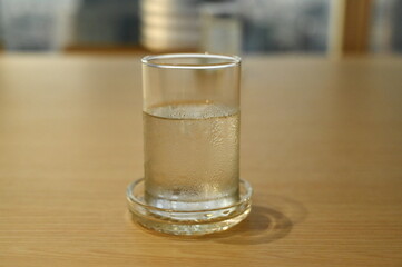 Water or completely defrosted mineral water in a clear glass covered with a drop of water on a wooden table. The water that has been drunk has left no full glass.
