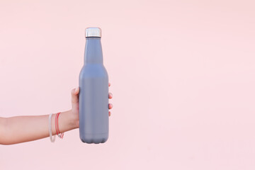 Close-up of female hand, holding a reusable, steel eco thermo water bottle of blue color. Pastel...