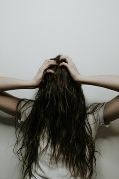 Stressed out woman with hair covering her face in front of a white wall