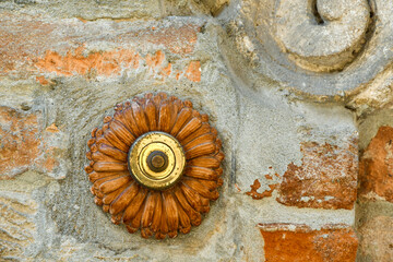 Close-up of an old terracotta doorbell in the shape of a flower on a weathered brick and stone wall, Italy