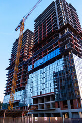 A crane at a high-rise building under construction. The construction site is fenced with warning...