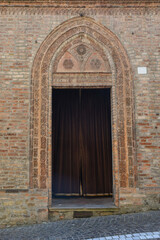 Close-up of the old entrance portal of a medieval church with a decorated brick frame and a velvet curtain, Italy
