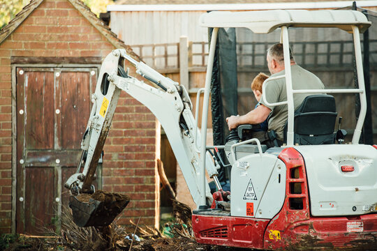 Annonymous man and boy using a digger in a back yard