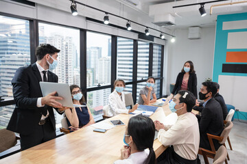 Caucasian businessman wearing face mask with presentation of business plan on laptop, Multi ethnic corporate business group meeting in new normal office