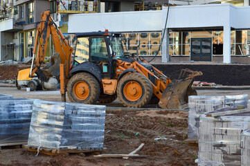 orange big excavator with black wheels at the construction site. appliances stand against the backdrop of a new glass house. around the stacked bricks covered with foil